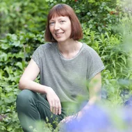 Ruth Reiche kniet in einem Garten und lächelt in die Kamera